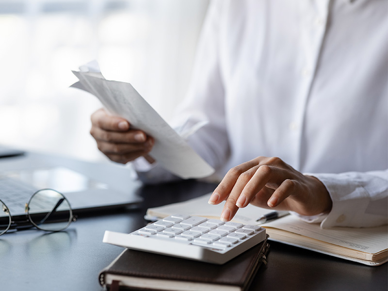 Female professional reviewing financial statements and making calculations on a calculator.